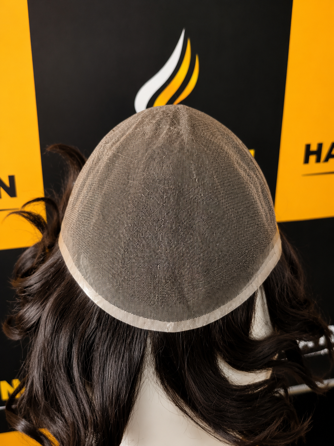 Mannequin head with a gray wig cap against a black and yellow background