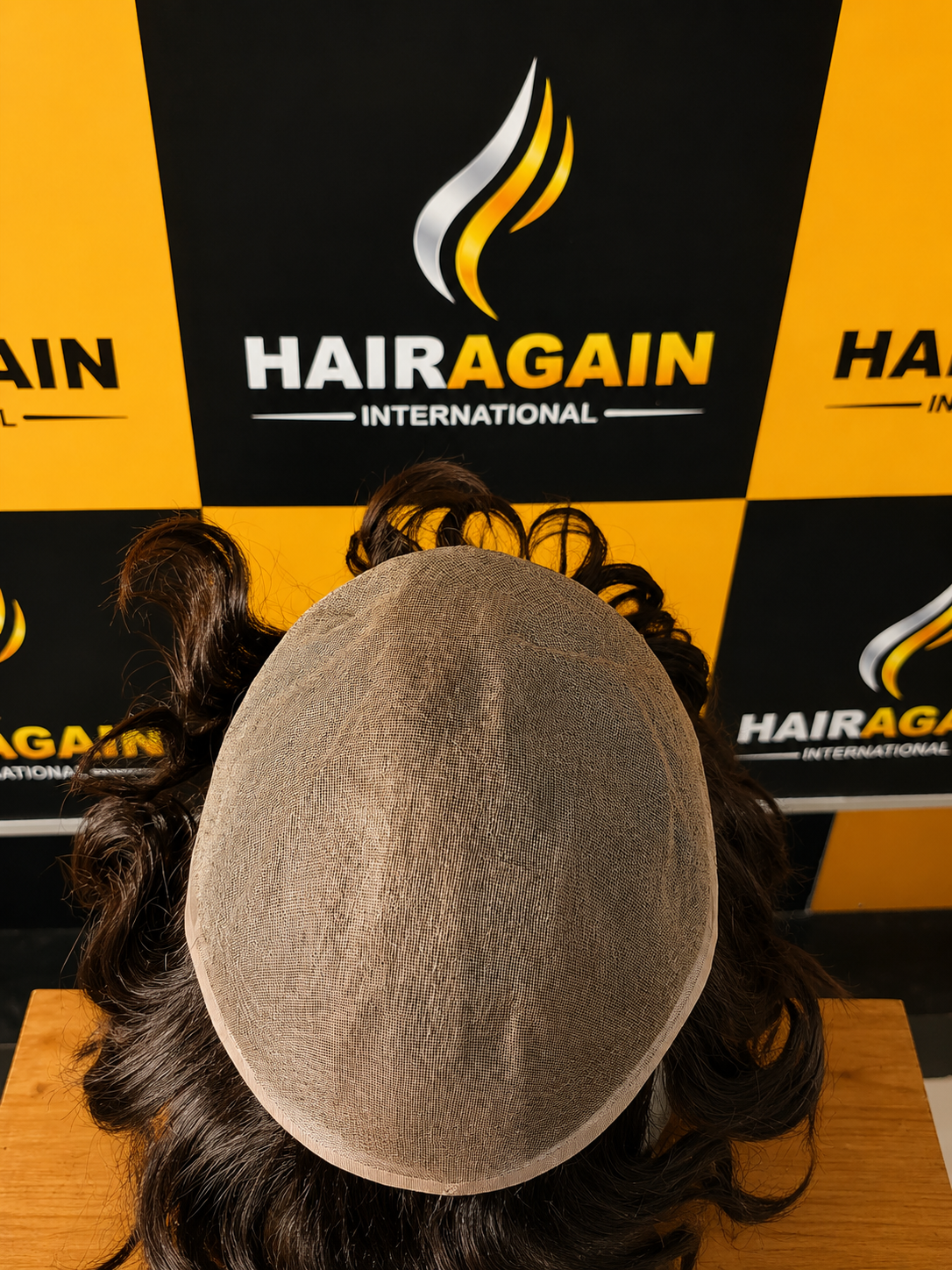 HairAgain International product display with a head model wearing a hairpiece against a branded backdrop.