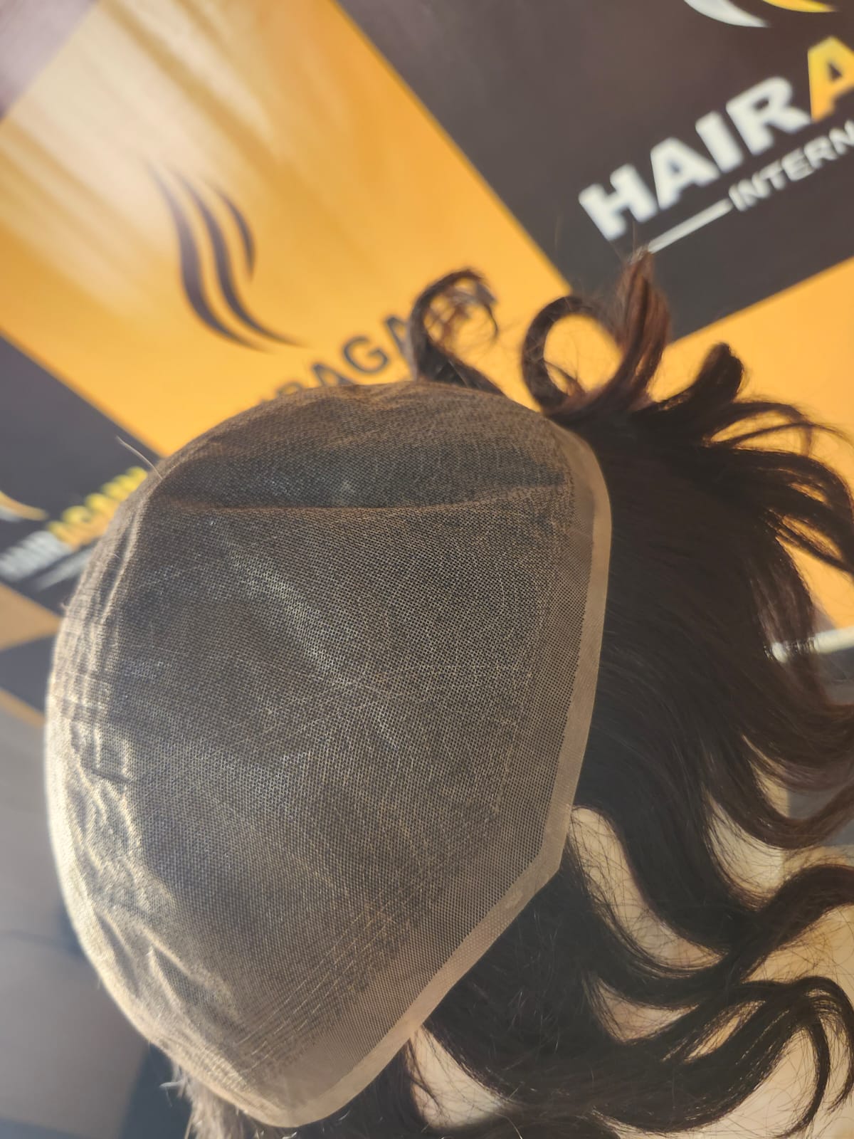 Hair extension on a mesh base with a blurred background featuring 'HAIR' branding.
